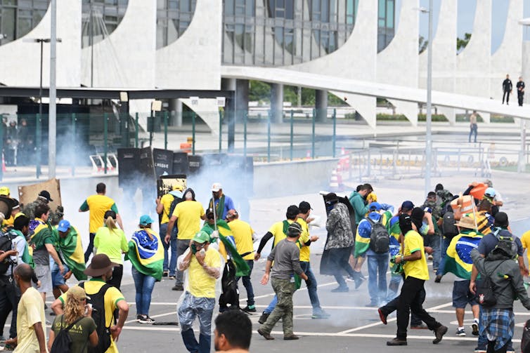 Homens e mulheres enchem uma rua com fumaça rodopiando ao redor.